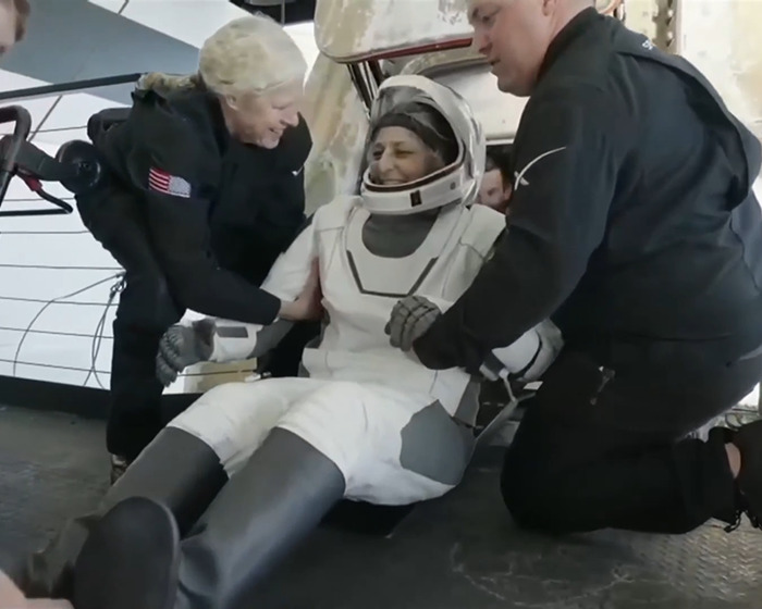 NASA astronaut being assisted after space mission, wearing a white spacesuit, showing signs of strain and relief. NASA astronaut being assisted after space mission, wearing a white spacesuit, showing signs of strain and relief.