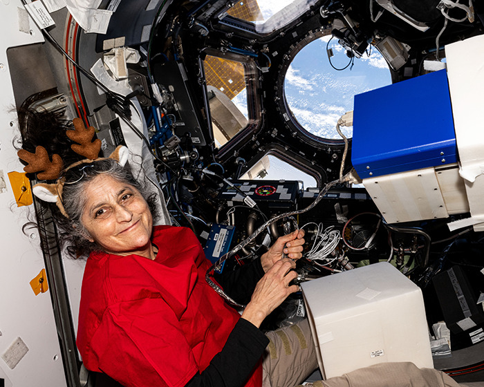 NASA astronaut in spacecraft, wearing festive antlers, with Earth visible through the window. NASA astronaut in spacecraft, wearing festive antlers, with Earth visible through the window.