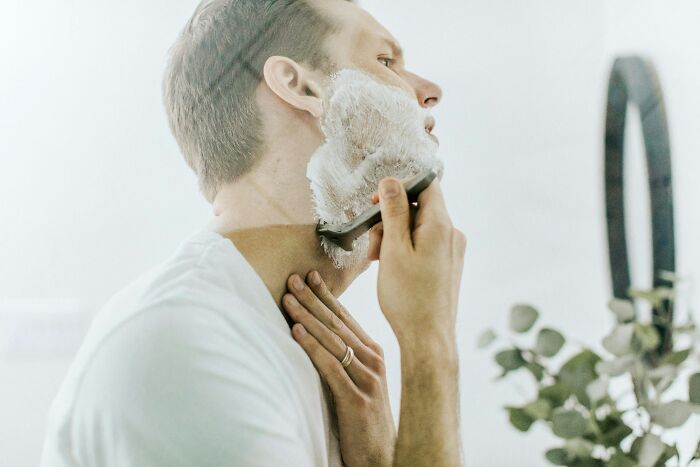 Man shaving his face in a bright bathroom, challenging common stereotypes about grooming habits.