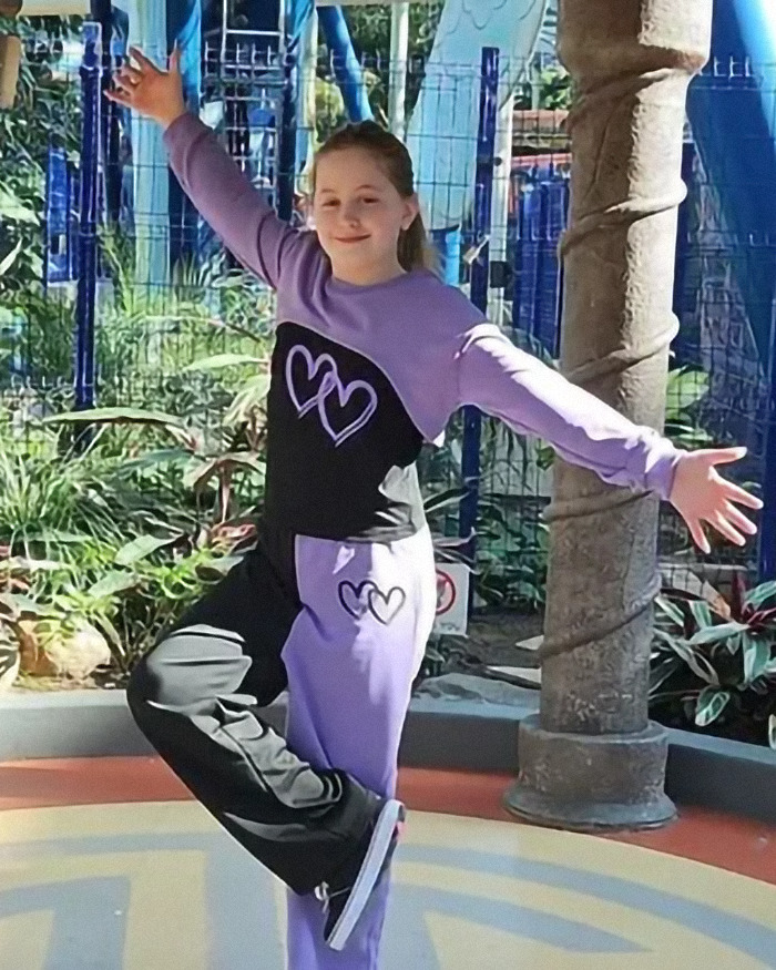 Lilyana Loycano in purple outfit posing with arms outstretched at a park, near plants and a tree pillar. Lilyana Loycano in purple outfit posing with arms outstretched at a park, near plants and a tree pillar.