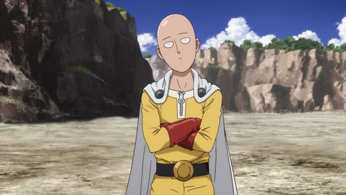 A bald superhero in a yellow suit standing confidently in a rocky landscape, embodying the concept of hyped up expectations.