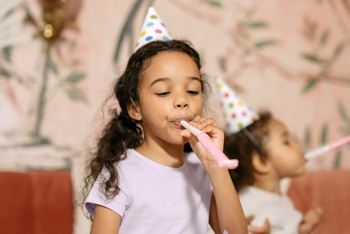 Children at a birthday party, wearing hats and blowing noisemakers, highlighting inclusion and celebration. Children at a birthday party, wearing hats and blowing noisemakers, highlighting inclusion and celebration.