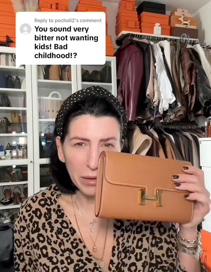 Millennial woman holding a designer clutch in a closet, responding to a critical comment about her child-free lifestyle choices. Millennial woman holding a designer clutch in a closet, responding to a critical comment about her child-free lifestyle choices.