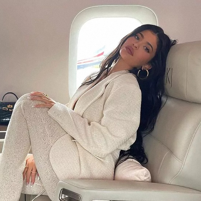 Woman in a cream outfit sitting in a luxurious airplane seat, with long dark hair and hoop earrings. Woman in a cream outfit sitting in a luxurious airplane seat, with long dark hair and hoop earrings.