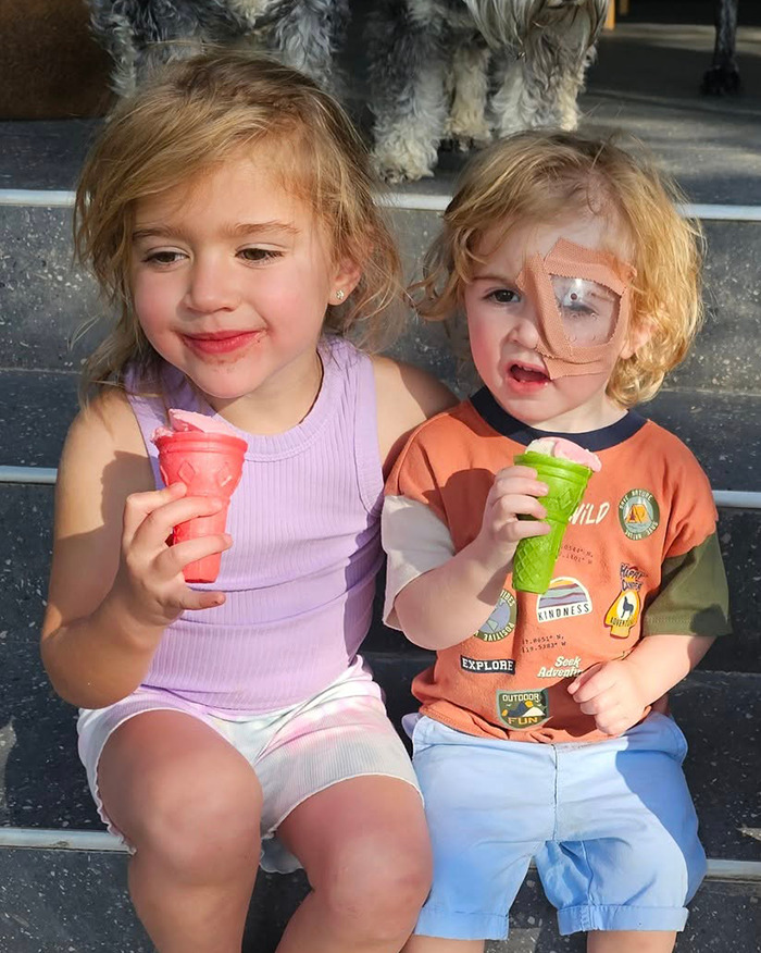 Toddler at risk of eye injury from herpes, wearing an eye patch, sitting with a girl, both holding ice cream cones. Toddler at risk of eye injury from herpes, wearing an eye patch, sitting with a girl, both holding ice cream cones.