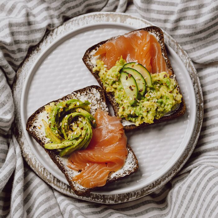 Avocado toast with smoked salmon, viewed on a striped cloth, questioning commonly misunderstood healthy foods.