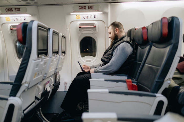 New hire on a flight, seated and looking at a phone, in a row with extra space for comfort. New hire on a flight, seated and looking at a phone, in a row with extra space for comfort.
