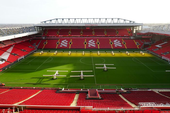 Anfield stadium, one of the cathedrals of soccer, with red stands and equipment on the green pitch for turf maintenance.