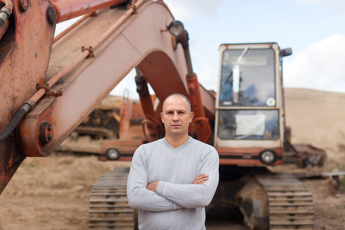 A person standing confidently in front of a large excavator on a construction site, showcasing unexpected things in reality.