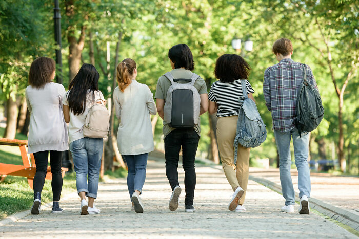 Group of diverse friends walking together on a tree-lined path, carrying backpacks, showcasing unexpected things in reality.