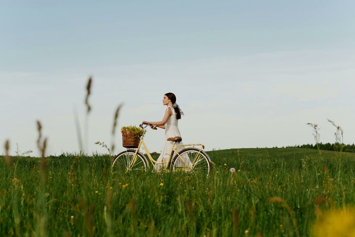 Woman with a bicycle in a green field, highlighting the unexpected beauty of reality.