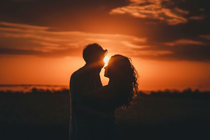 A couple silhouetted against a sunset, embracing in a romantic reality moment.