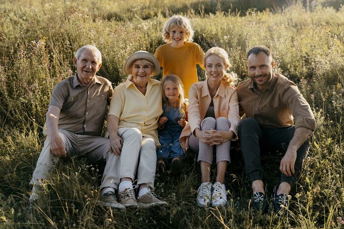 Family sitting on grass in a field, smiling and enjoying an outdoor moment, showcasing unexpected things in reality.