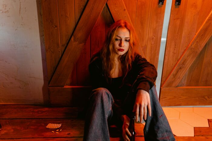 A woman sitting on a wooden floor, looking contemplative, holding a bottle, capturing unexpected reality moments.