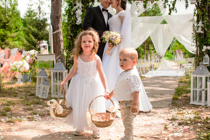 Kids at a wedding, two children with baskets, bride and groom in background, outdoors. Kids at a wedding, two children with baskets, bride and groom in background, outdoors.