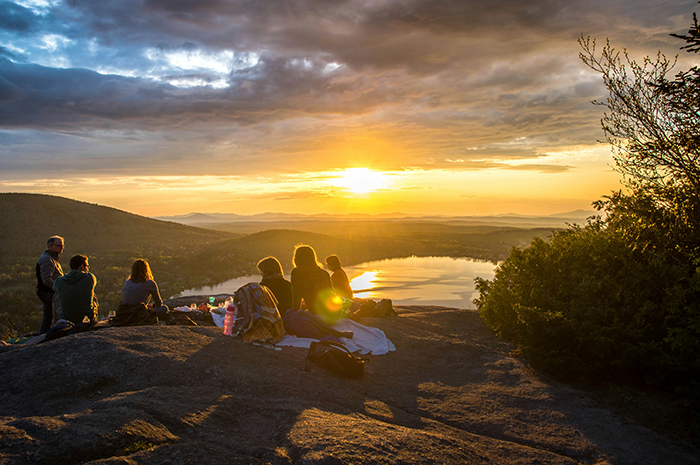 Group enjoying a sunset view by a lake, seated on a scenic hilltop. Group enjoying a sunset view by a lake, seated on a scenic hilltop.