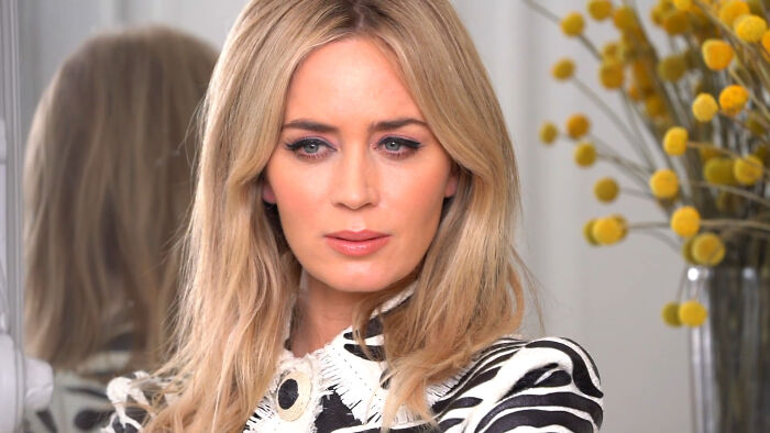 Blonde celebrity in a stylish black and white outfit, with yellow flowers in the background.