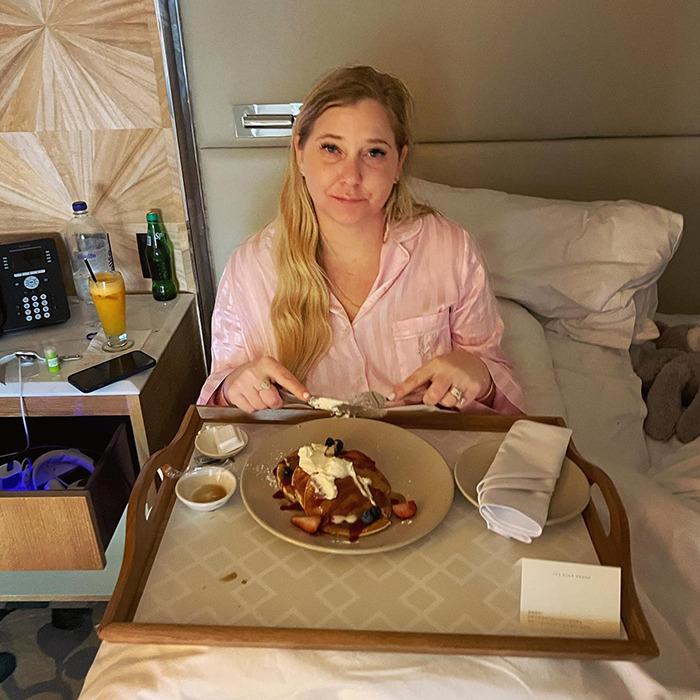 Woman in pink pajamas eating breakfast in bed, near a phone and drink, related to Prince Andrew's accuser incident. Woman in pink pajamas eating breakfast in bed, near a phone and drink, related to Prince Andrew's accuser incident.