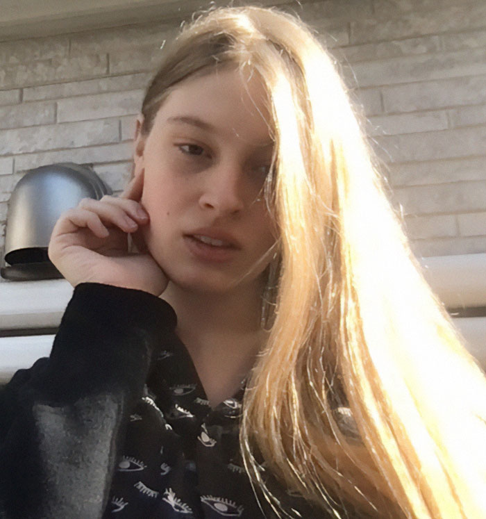 Person with long blond hair, wearing a patterned top, sitting outdoors in sunlight. Person with long blond hair, wearing a patterned top, sitting outdoors in sunlight.