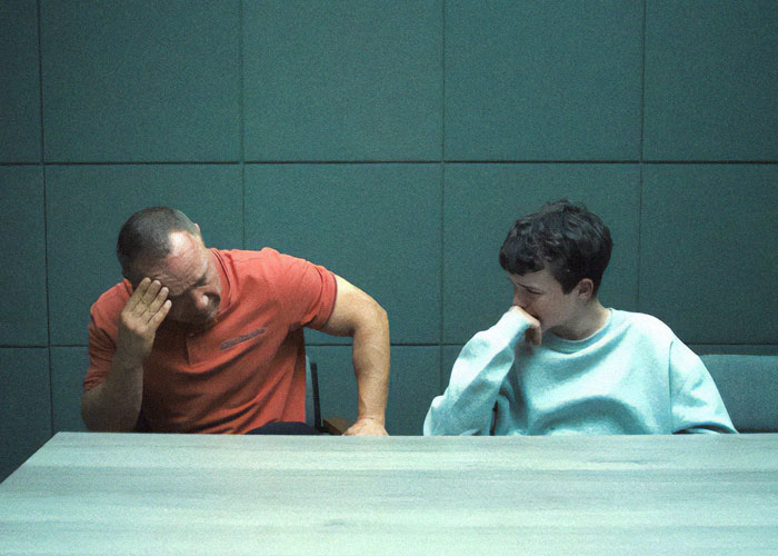 Two people sitting at a table, looking contemplative, related to "Adolescence" TV show's emoji theme. Two people sitting at a table, looking contemplative, related to "Adolescence" TV show's emoji theme.