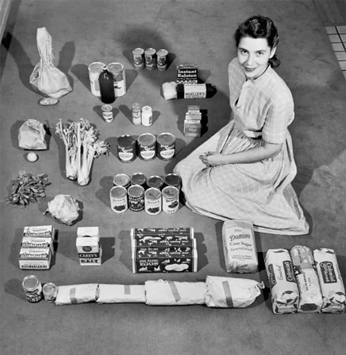 A woman in vintage clothing sits with 1950s American groceries arranged on the floor, showcasing everyday life in the past. A woman in vintage clothing sits with 1950s American groceries arranged on the floor, showcasing everyday life in the past.