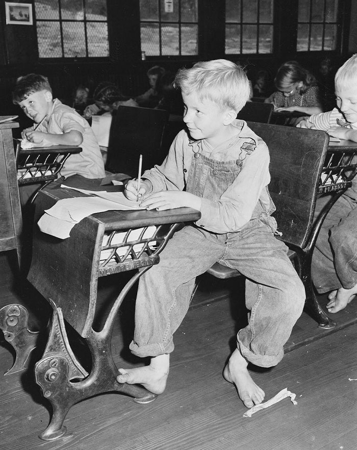 A vintage classroom scene showing American children writing at wooden desks, capturing historical everyday life. A vintage classroom scene showing American children writing at wooden desks, capturing historical everyday life.