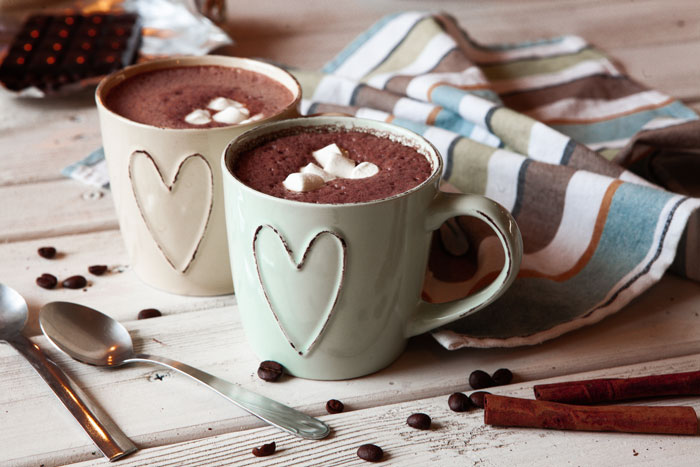 Two heart-adorned mugs of hot chocolate on a wooden table with scattered coffee beans and cinnamon sticks. Two heart-adorned mugs of hot chocolate on a wooden table with scattered coffee beans and cinnamon sticks.