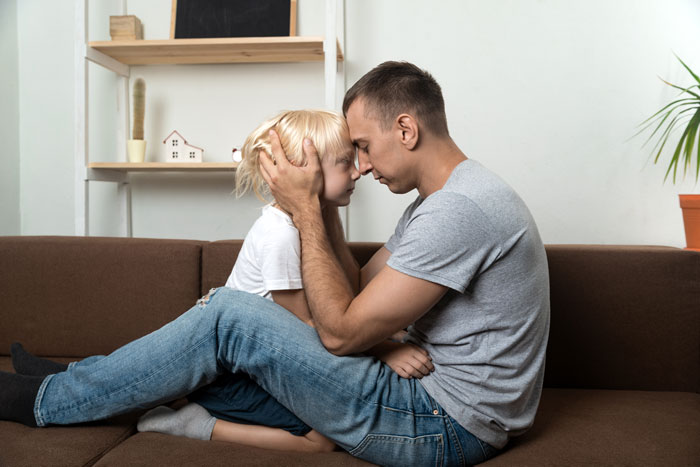 Dad comforting his child on a couch, expressing concern and support during a difficult family situation. Dad comforting his child on a couch, expressing concern and support during a difficult family situation.