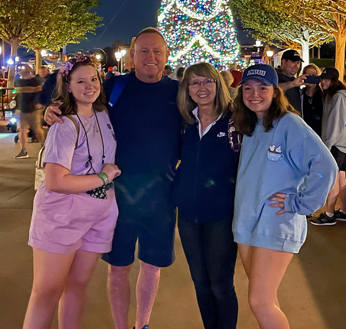 Astronaut's daughter with family, smiling by a lit Christmas tree at night, highlighting concerns for health. Astronaut's daughter with family, smiling by a lit Christmas tree at night, highlighting concerns for health.