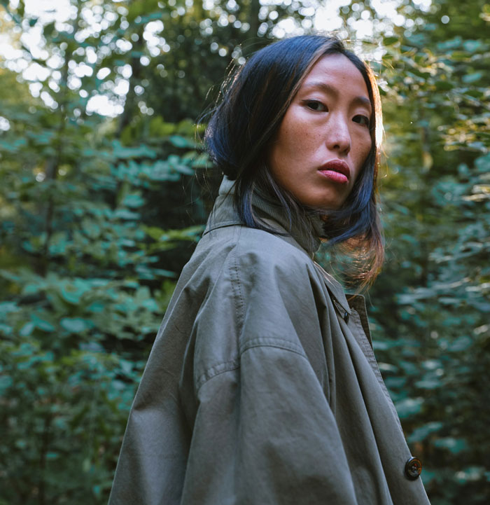 A woman in a green coat looking over her shoulder in a forest setting, related to child services inquiry. A woman in a green coat looking over her shoulder in a forest setting, related to child services inquiry.