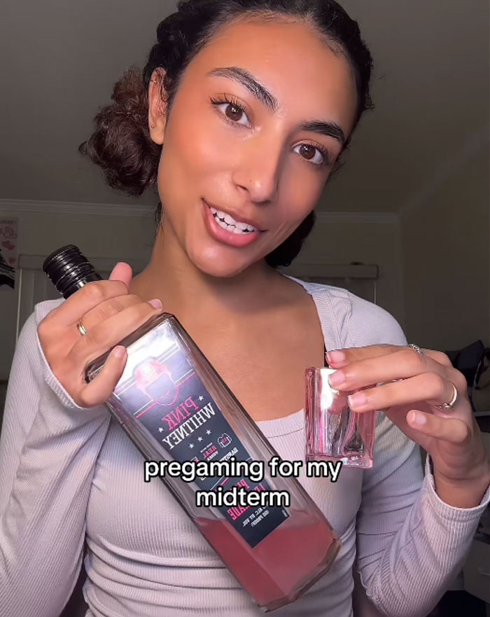 College student pregaming with a bottle, smiling, holding a glass, possibly preparing for a midterm. College student pregaming with a bottle, smiling, holding a glass, possibly preparing for a midterm.