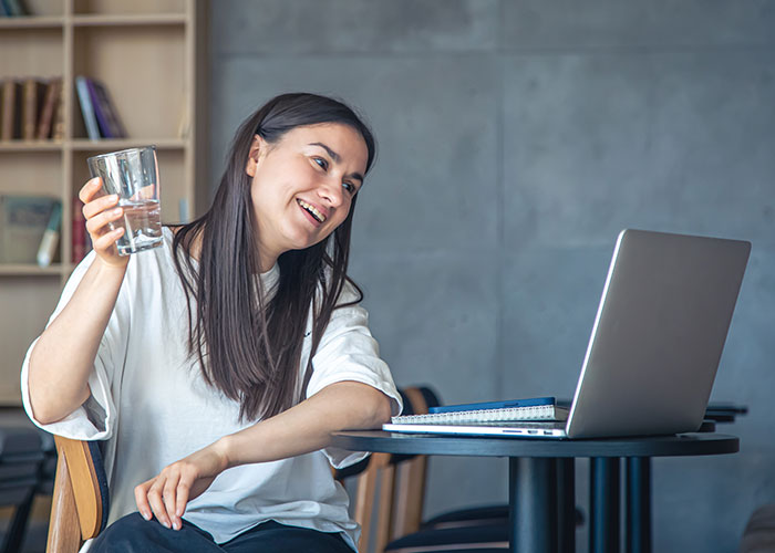 College student pregaming midterm online, holding a drink, and smiling at her laptop. College student pregaming midterm online, holding a drink, and smiling at her laptop.