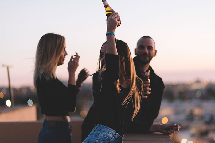 Three people enjoying drinks on a rooftop at sunset, with an urban view in the background. Three people enjoying drinks on a rooftop at sunset, with an urban view in the background.