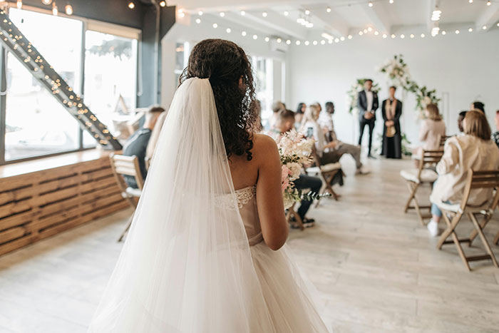 Bride walking down the aisle at a wedding, decorated with flowers and lights, guests seated. Bride walking down the aisle at a wedding, decorated with flowers and lights, guests seated.