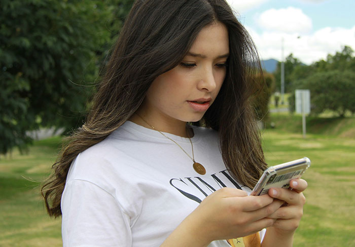 Young woman in a white shirt looking at her phone, standing in a park. Young woman in a white shirt looking at her phone, standing in a park.