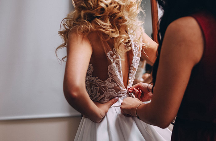 Woman in wedding dress being helped with buttons, questions wedding after fiancé sides with sister. Woman in wedding dress being helped with buttons, questions wedding after fiancé sides with sister.