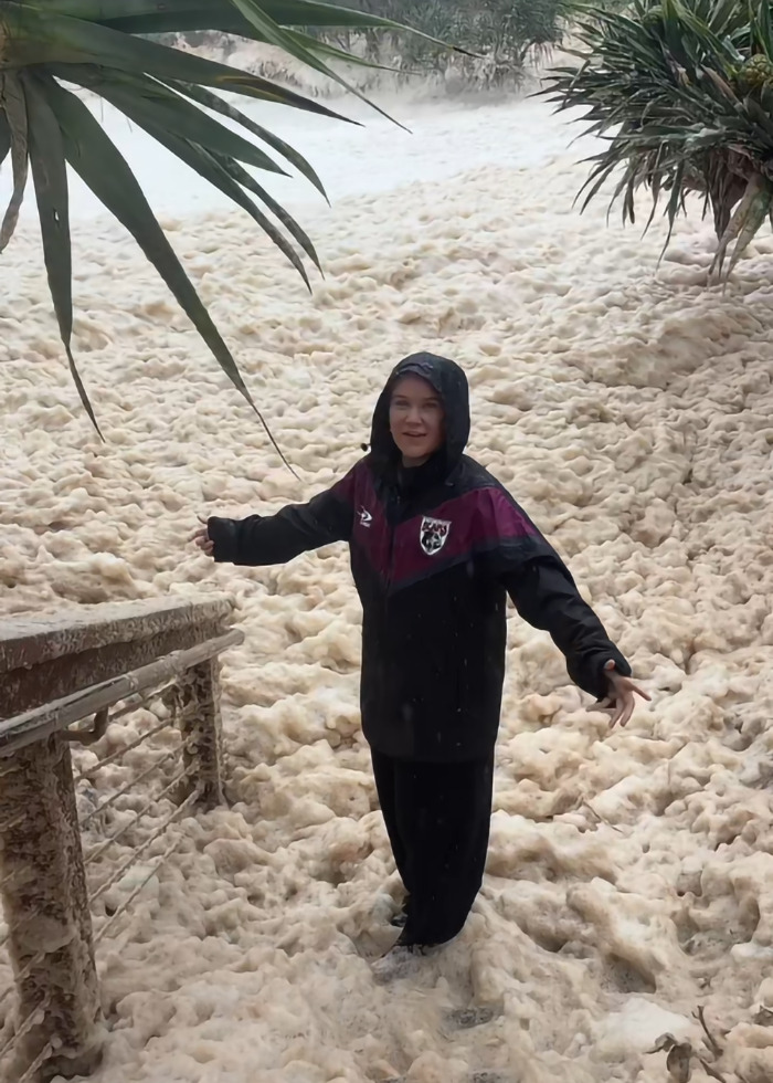 Woman in dark jacket standing amidst sewage-filled sea foam near a railing. Woman in dark jacket standing amidst sewage-filled sea foam near a railing.