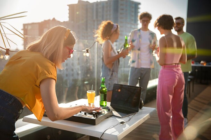 A woman DJ at a work party with guests holding bottles, unaware the punch is non-alcoholic. A woman DJ at a work party with guests holding bottles, unaware the punch is non-alcoholic.