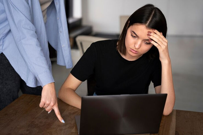 Woman looking embarrassed at laptop while colleague points at screen in office setting. Woman looking embarrassed at laptop while colleague points at screen in office setting.