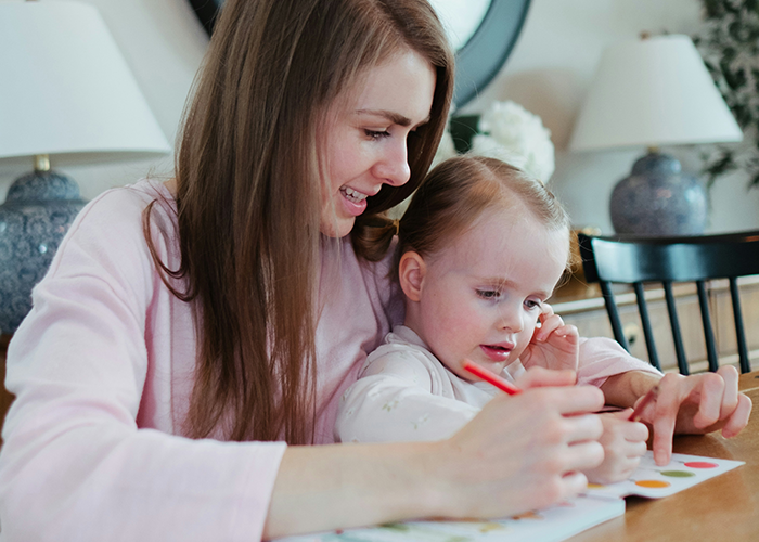 Woman practicing gentle parenting, guiding a toddler with coloring, sitting in a cozy home setting. Woman practicing gentle parenting, guiding a toddler with coloring, sitting in a cozy home setting.