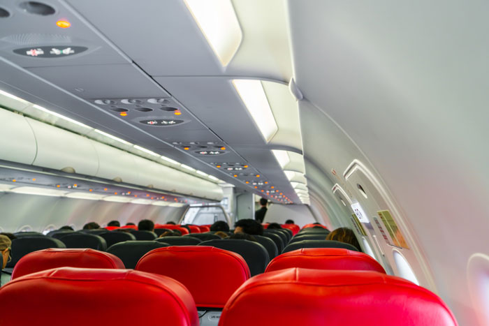 Passengers seated inside an airplane cabin, viewed from the rear, with red and black seats, suggesting in-flight drama. Passengers seated inside an airplane cabin, viewed from the rear, with red and black seats, suggesting in-flight drama.