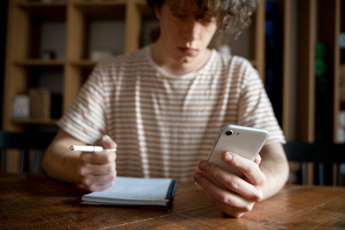 Young adult in a striped shirt looking at phone, contemplating experiences akin to being picked last.