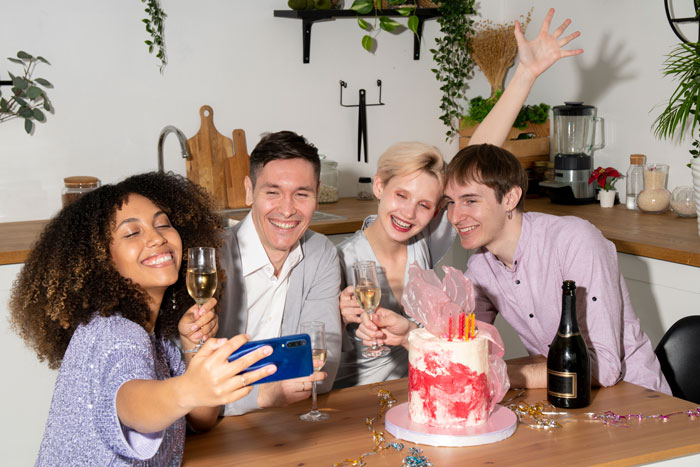 Four friends celebrating with a birthday cake and champagne, smiling for a selfie. Four friends celebrating with a birthday cake and champagne, smiling for a selfie.