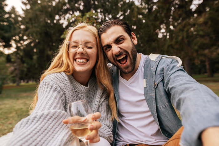Woman with man's crush, both smiling outdoors, holding a glass, enjoying a sunny day. Woman with man's crush, both smiling outdoors, holding a glass, enjoying a sunny day.