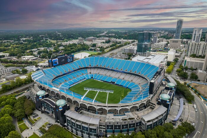 Aerial view of a large soccer cathedral stadium with blue seats and a green field in an urban area.