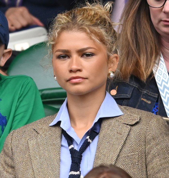 Woman in a herringbone blazer and blue shirt at an outdoor event, looking serious. Woman in a herringbone blazer and blue shirt at an outdoor event, looking serious.