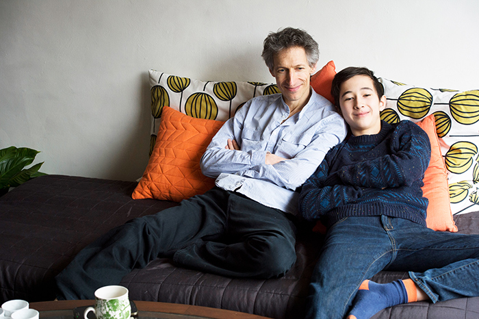 Father and teen boy lounging on a couch, snuggling against colorful cushions in a cozy living room. Father and teen boy lounging on a couch, snuggling against colorful cushions in a cozy living room.