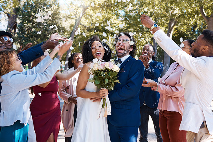 Bride and groom celebrate with guests throwing petals, outdoors after wedding ceremony. Bride and groom celebrate with guests throwing petals, outdoors after wedding ceremony.