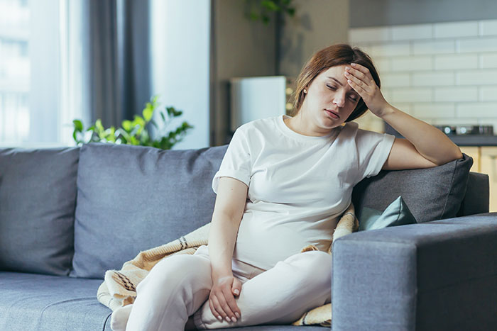 Pregnant woman on a couch, looking stressed in a modern living room setting. Pregnant woman on a couch, looking stressed in a modern living room setting.