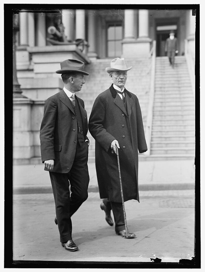 Two men in early 20th century attire walking outside a historic building, rare photograph rescued from glass negatives